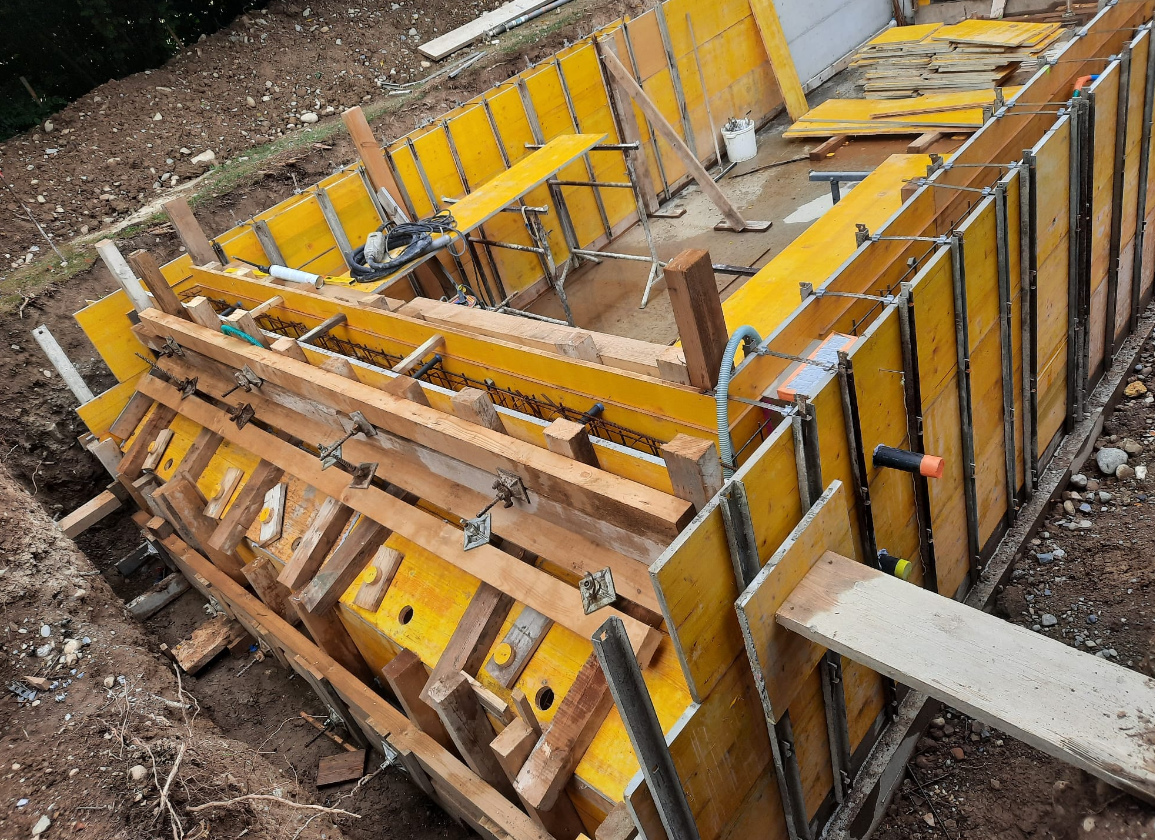 Gestellte gelbe Schalung mit Bewehrung für eine Betonwand auf einer Baustelle